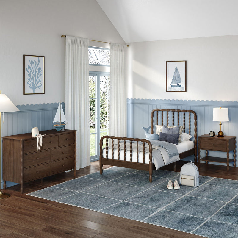 Coastal-themed children's bedroom with wooden spindle bed, blue wainscoting, dark wood dresser, sailboat wall art, plush whale, gray-blue area rug and white curtains
