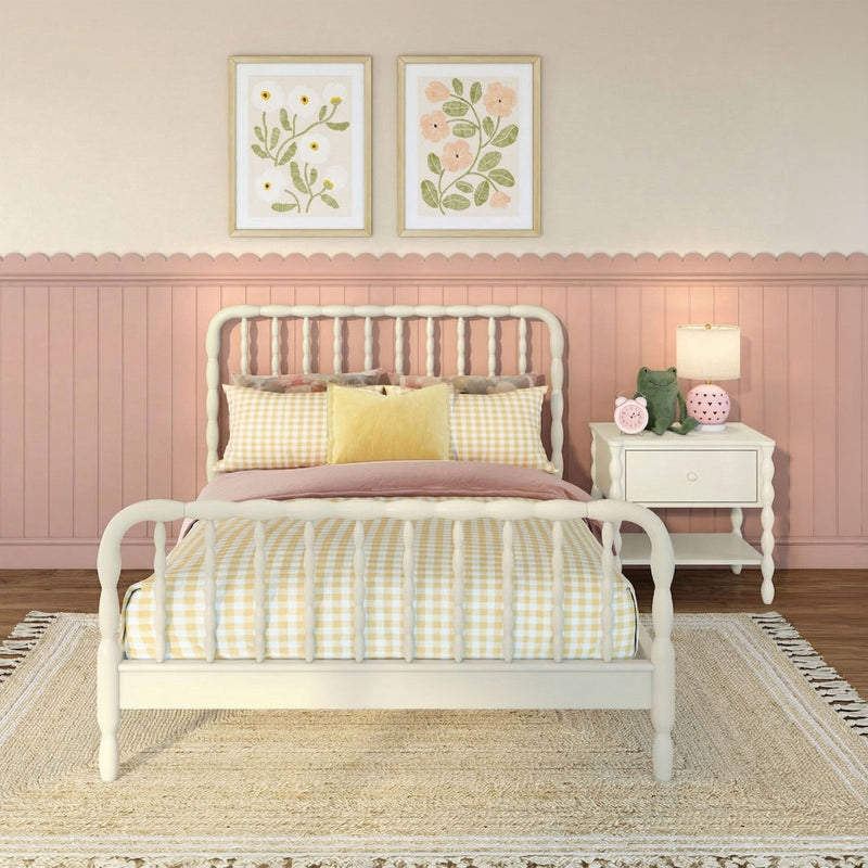Pastel pink girls nursery with white spindle bed, yellow gingham bedding, scalloped wainscoting, floral framed prints, bedside lamp and plush toys