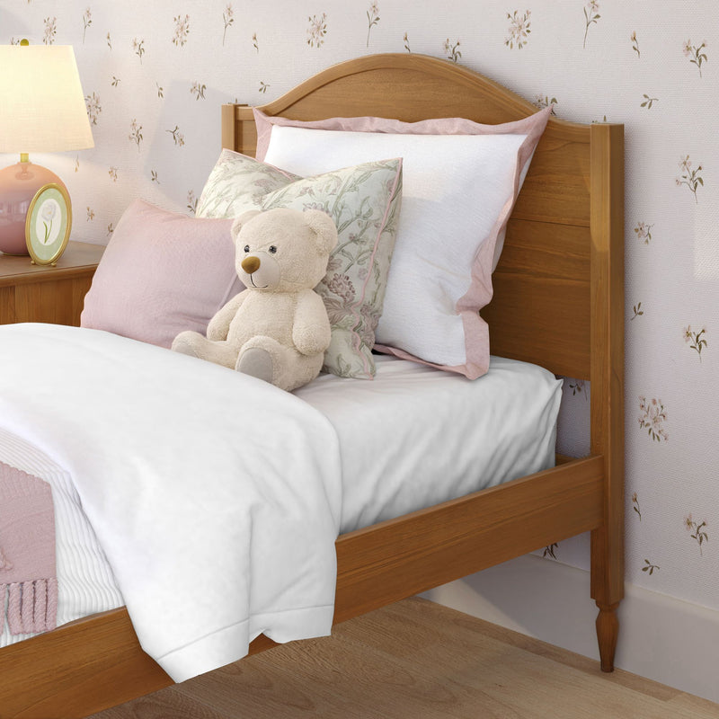 Cozy children's bedroom with wooden bed, white and pink bedding, floral throw pillows, plush teddy bear and bedside lamp