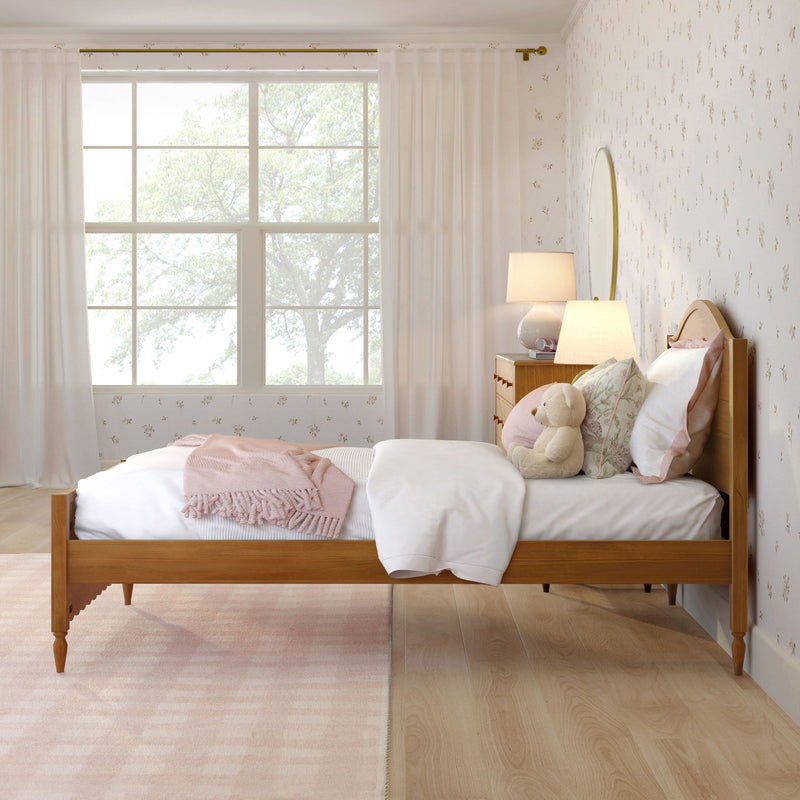 Cozy pastel girl's bedroom with wooden bed, pink throw blanket, plush teddy bear, bedside lamp, floral wallpaper and large window with sheer curtains