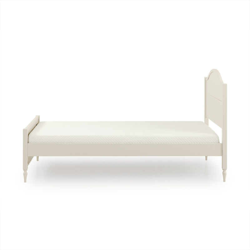 Cream wooden twin bed frame with scalloped headboard and quilted mattress on white background, minimalist bedroom furniture product photo