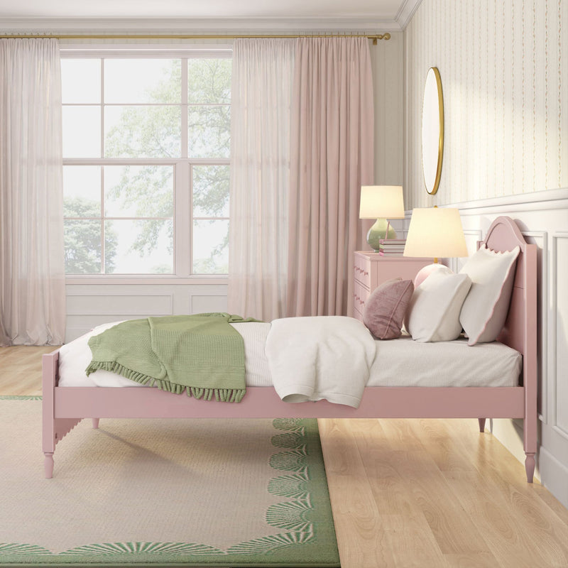 Pastel pink kids bedroom decor with pink wooden bed, white bedding, green knit throw, sheer window curtains, bedside lamps and round gold mirror