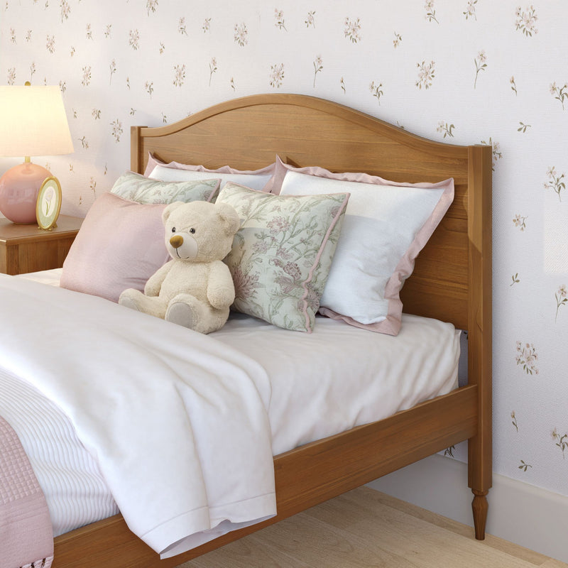 Cozy girl's bedroom with wooden twin bed, pastel pink bedding, floral throw pillows, plush teddy bear and bedside lamp against floral wallpaper
