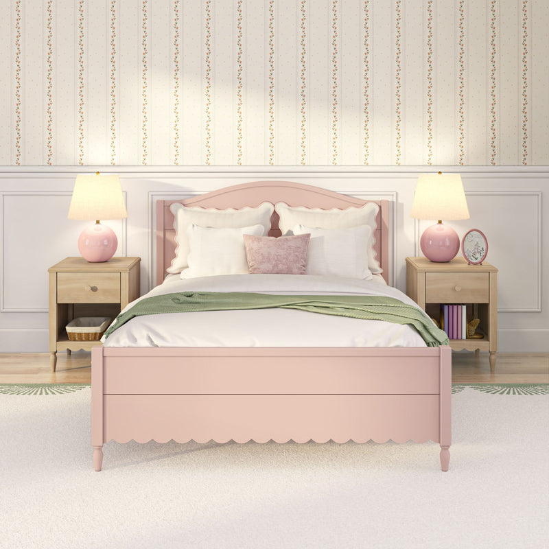 Pastel pink bedroom with scalloped bed, white pillows, green throw, wooden nightstands and pink lamps against floral wallpaper