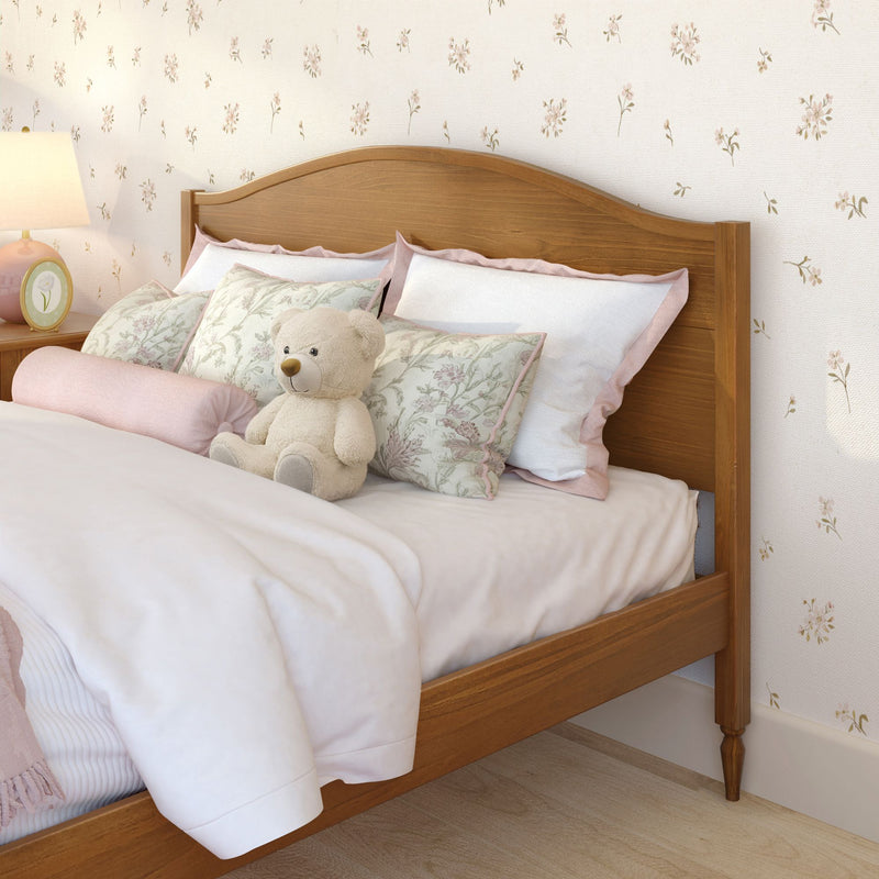 Cozy nursery bedroom with wooden headboard, pastel pink floral bedding and pillows, plush teddy bear, bedside lamp and floral wallpaper