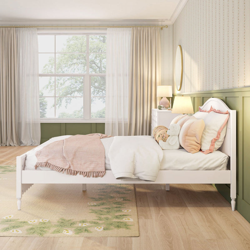Kids bedroom with white bed frame, pastel pink bedding and throw, green paneled headboard, bedside lamp and window with sheer curtains