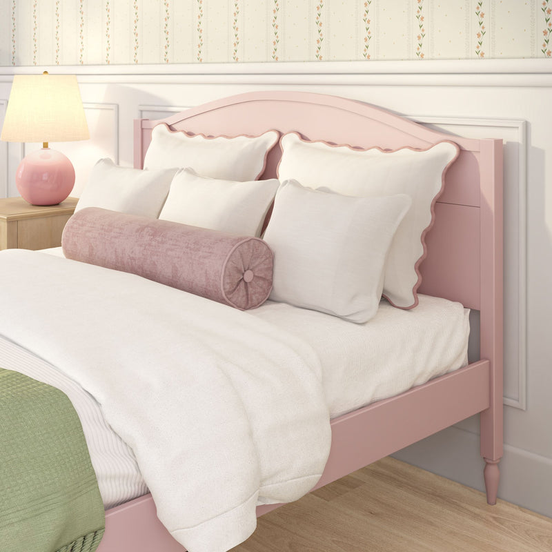 Pastel pink scalloped headboard bed with white decorative pillows and pink bolster, pink ceramic lamp on wooden nightstand and floral wallpaper