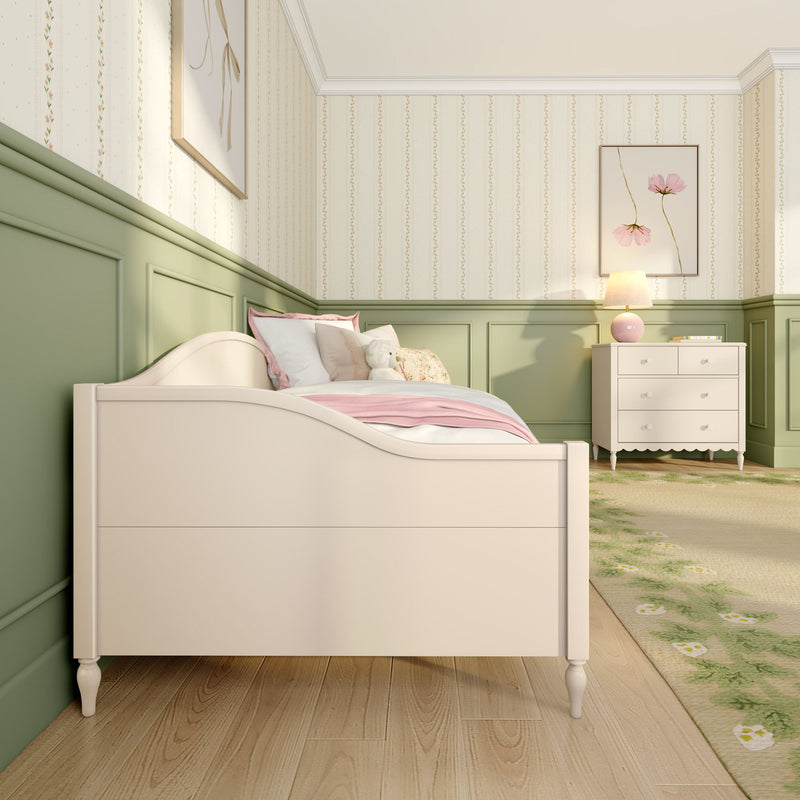 Girls bedroom nursery with cream wooden bed, pink bedding and teddy bear, pastel green wainscoting, floral wallpaper, and white dresser with lamp