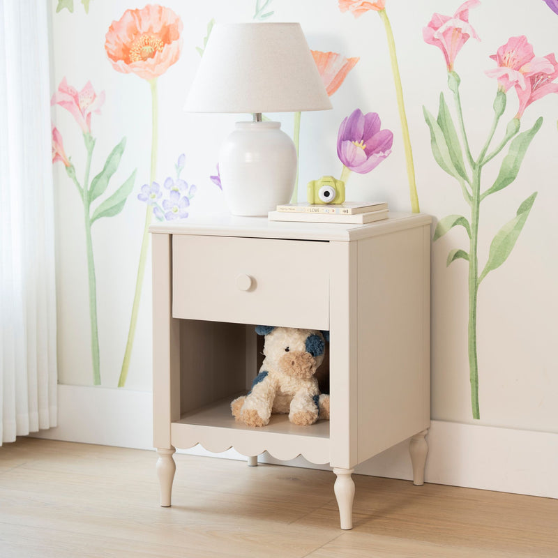 Pastel nursery nightstand with white ceramic lamp, floral watercolor wallpaper, stack of children's books, yellow toy camera and teddy bear