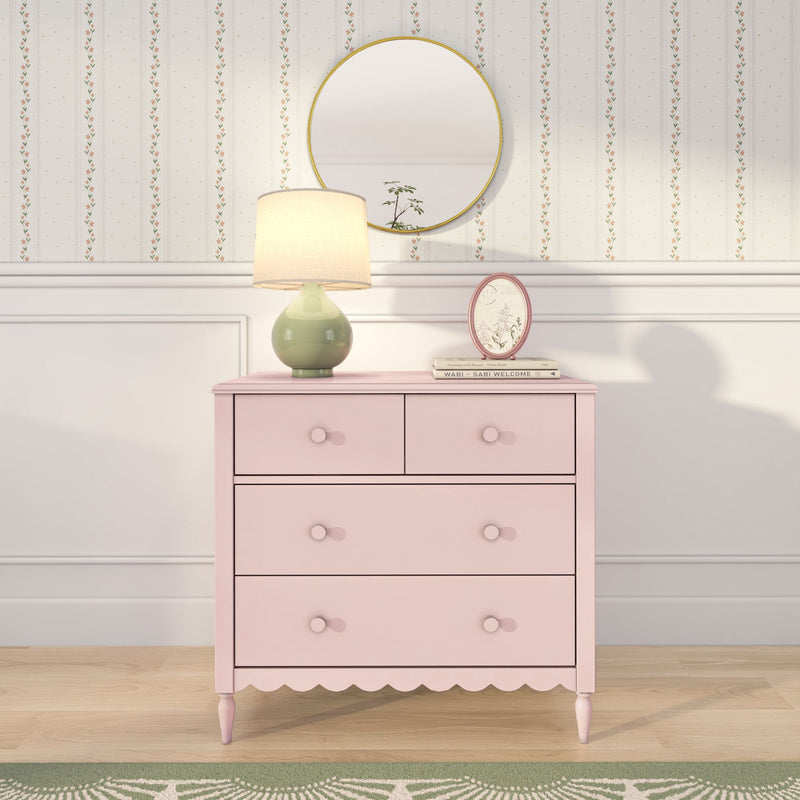 Pastel pink dresser with green ceramic table lamp, round gold mirror and floral striped wallpaper in a shabby-chic nursery bedroom decor scene