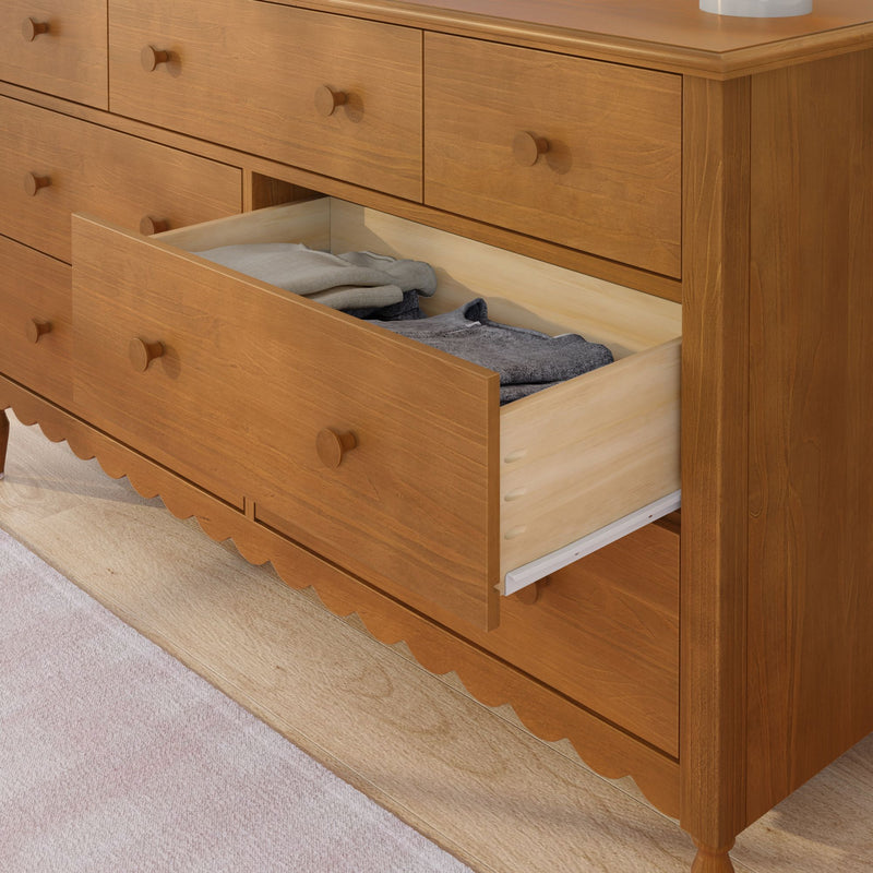 Honey oak wooden dresser with round knobs and an open drawer revealing neatly folded clothes on the floor, classic chest of drawers for bedroom storage and organization