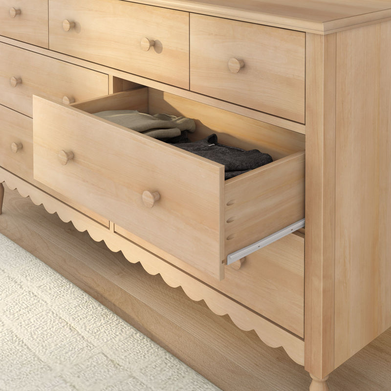 Light wooden dresser with open drawer and folded clothes, bedroom chest of drawers with round knobs and natural wood finish on hardwood floor