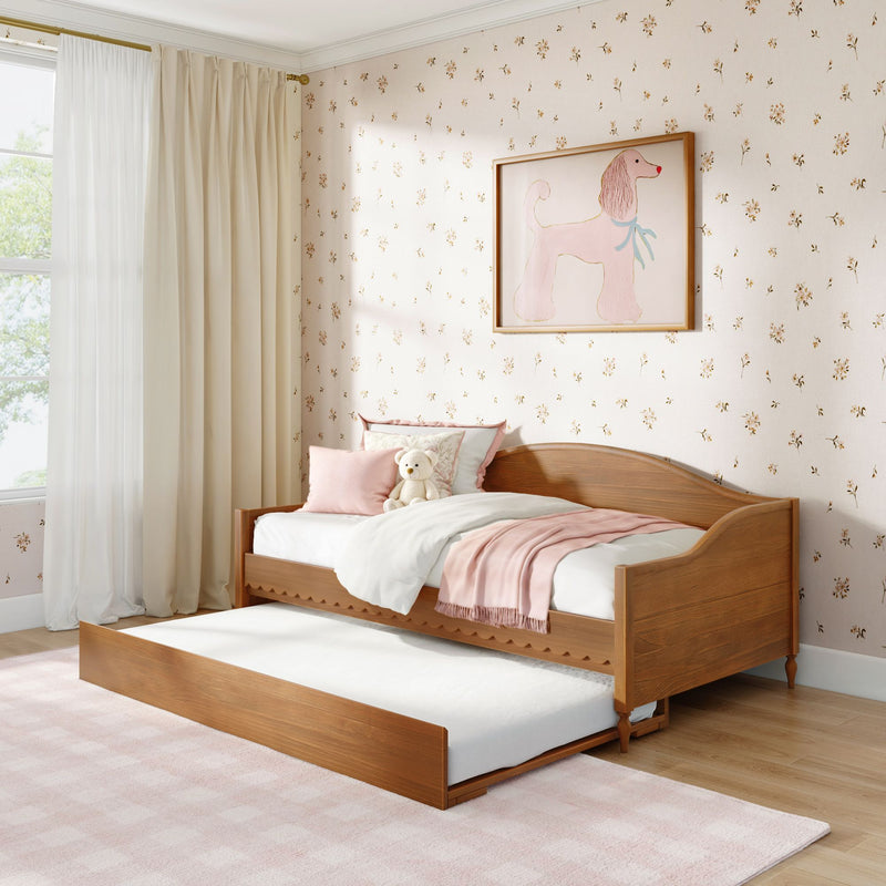 Children's bedroom with wooden twin trundle bed, pink bedding and pillows, plush teddy bear, floral wallpaper, framed poodle art and cream curtains