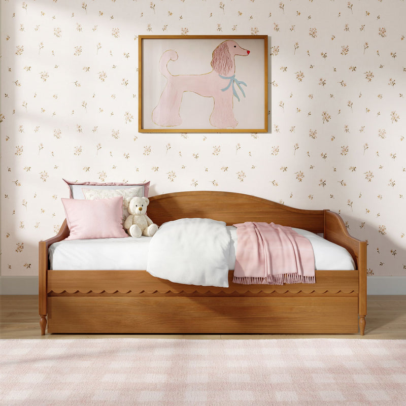 Cozy girls bedroom with wooden daybed, pastel pink bedding and throw, plush teddy bear, floral wallpaper and framed pink poodle wall art