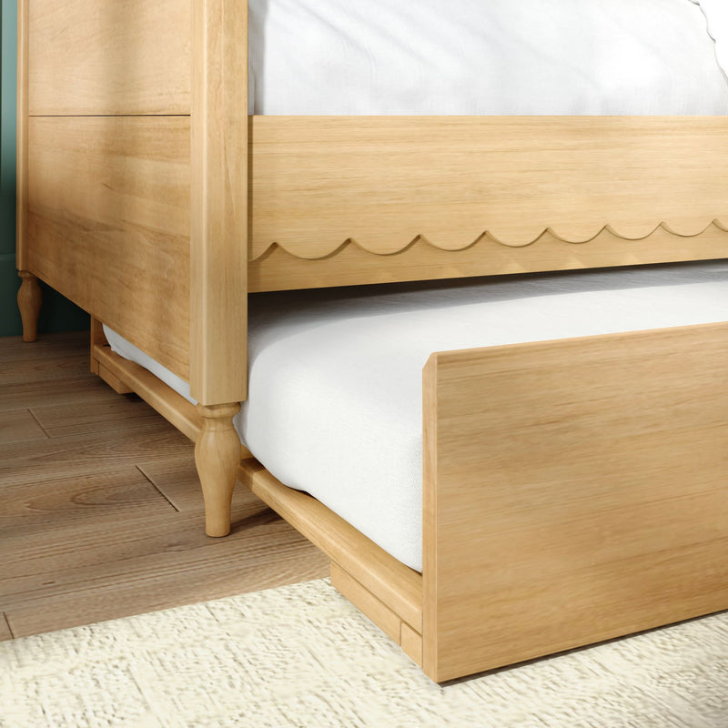Close-up of natural light wood bed frame with scalloped apron, turned legs and white mattress on hardwood floor