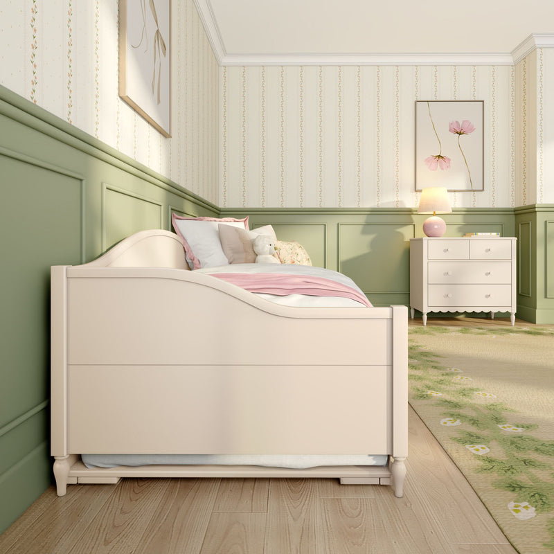 Cozy pastel girls nursery with white toddler bed and pink bedding, stuffed bear, green wainscoting, floral wallpaper and white dresser with lamp — stylish children's bedroom interior