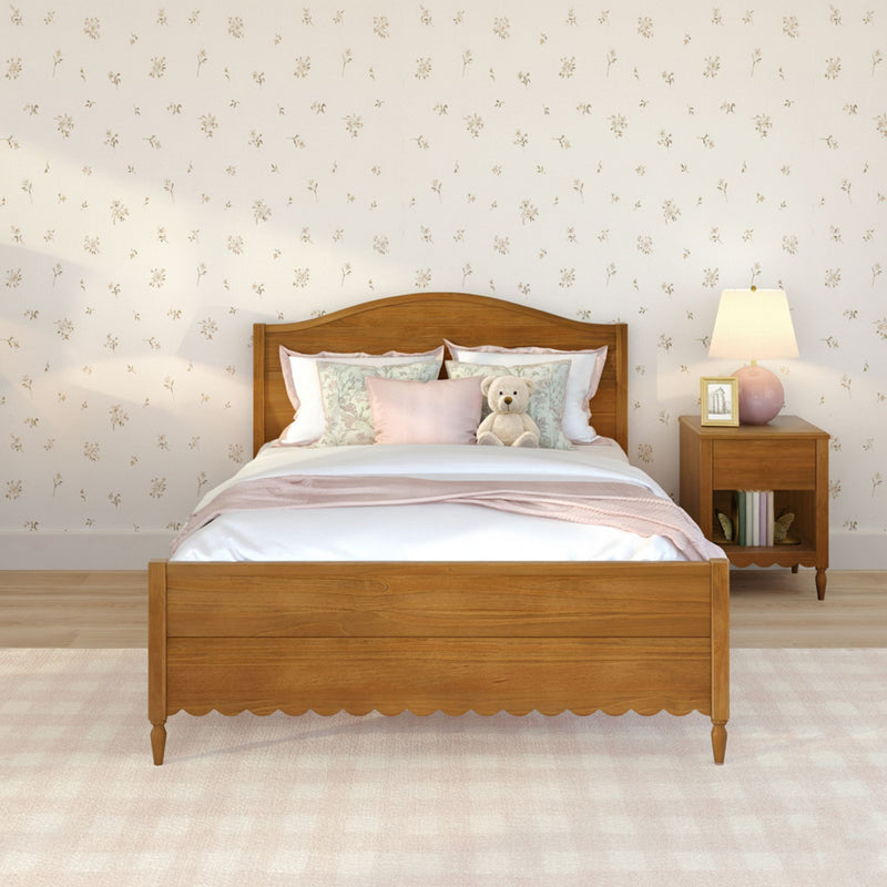 Wooden bed with pink bedding, teddy bear on pillows, floral wallpaper, wooden nightstand with lamp and framed photo, soft plush carpet