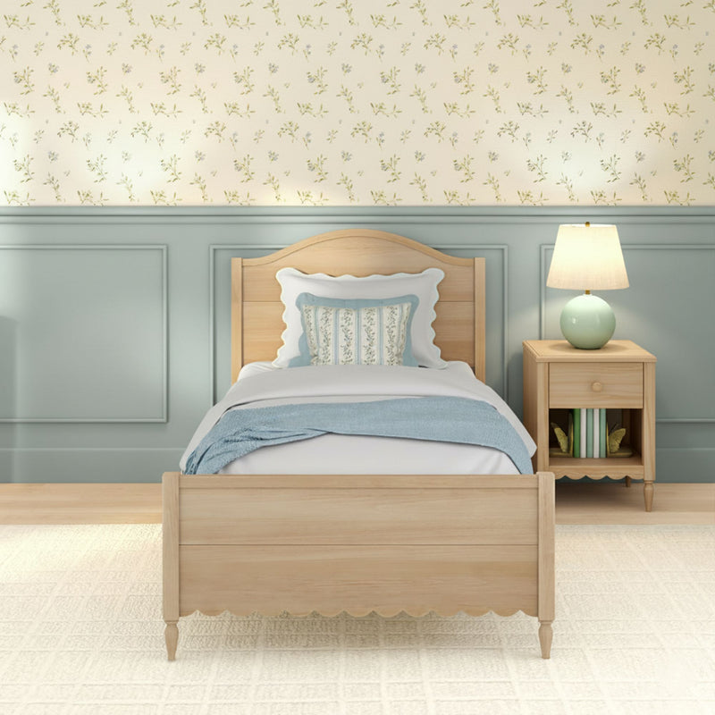Cozy coastal cottage bedroom with light wood twin bed, pastel blue wainscoting, delicate floral wallpaper, patterned pillows and bedside table lamp