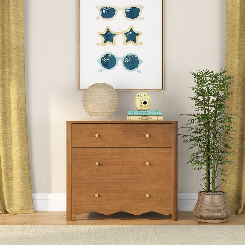 Warm oak four-drawer wooden dresser with brass knobs, paper lantern lamp and yellow instant camera on books, framed sunglasses wall art, potted bamboo and mustard curtains, stylish bedroom decor