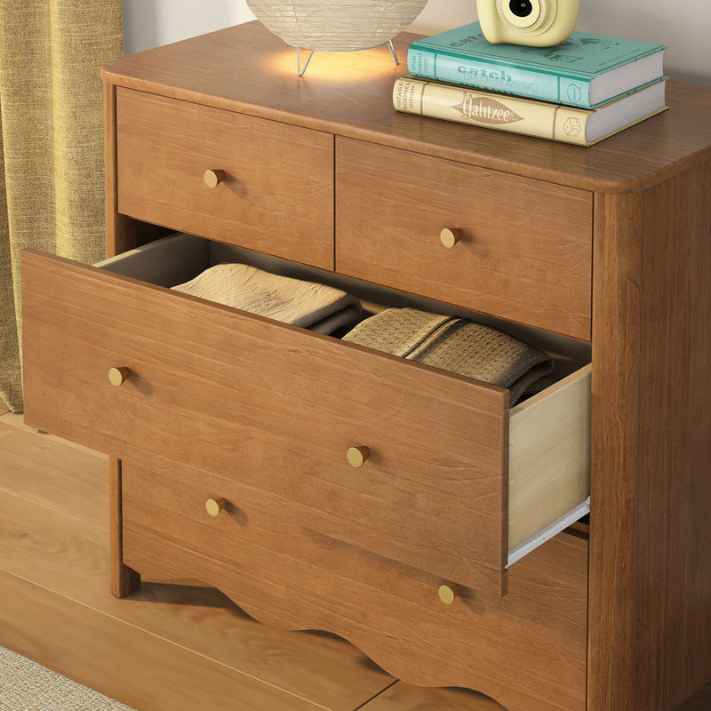 Solid wood mid-century dresser with open drawer revealing folded blankets, brass knobs, lamp and stacked books on top — bedroom storage and decor