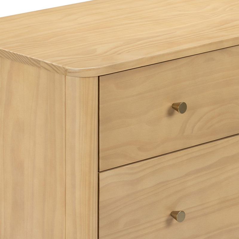 Close-up of modern light pine dresser with natural wood grain finish, smooth rounded top edge and brass drawer knob.