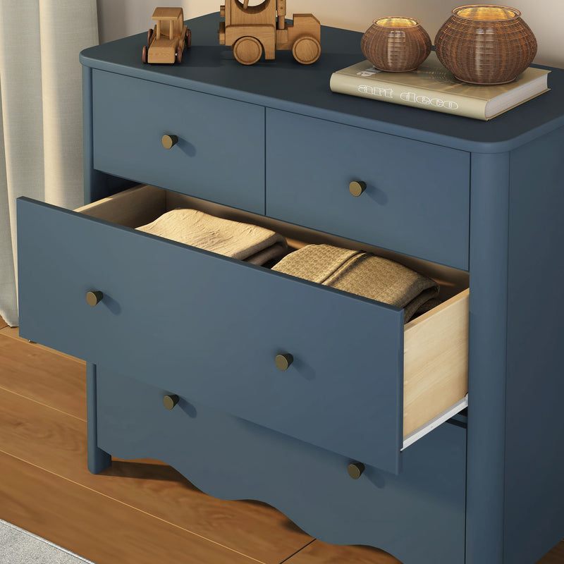 Blue wooden dresser with open drawer revealing folded blankets, brass knobs, wooden toy cars and wicker candle holders on top, staged on hardwood floor