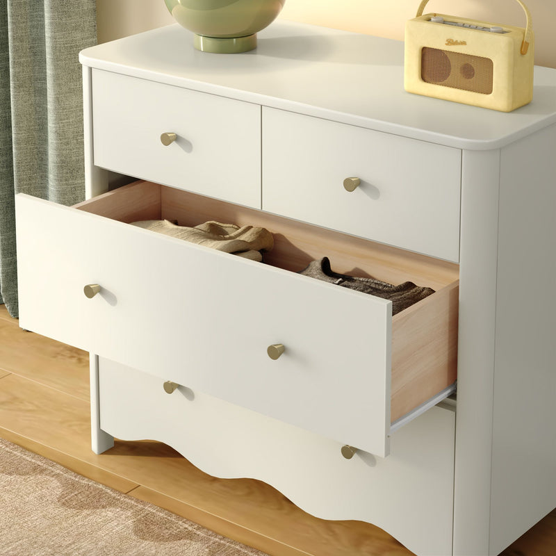 White dresser with open drawer revealing folded clothes, brass knobs and wood interior, styled with green lamp and retro yellow radio for minimalist bedroom decor