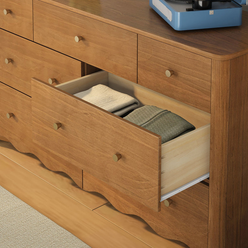 Mid-century modern wooden dresser with brass knobs, open drawer of folded clothes and a blue record player on top, bedroom storage furniture