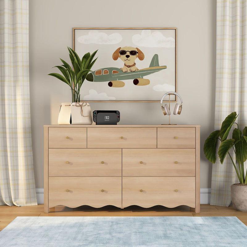 Light wood 6-drawer nursery dresser styled with airplane dog wall art, potted plants, headphones, gaming console and soft blue rug