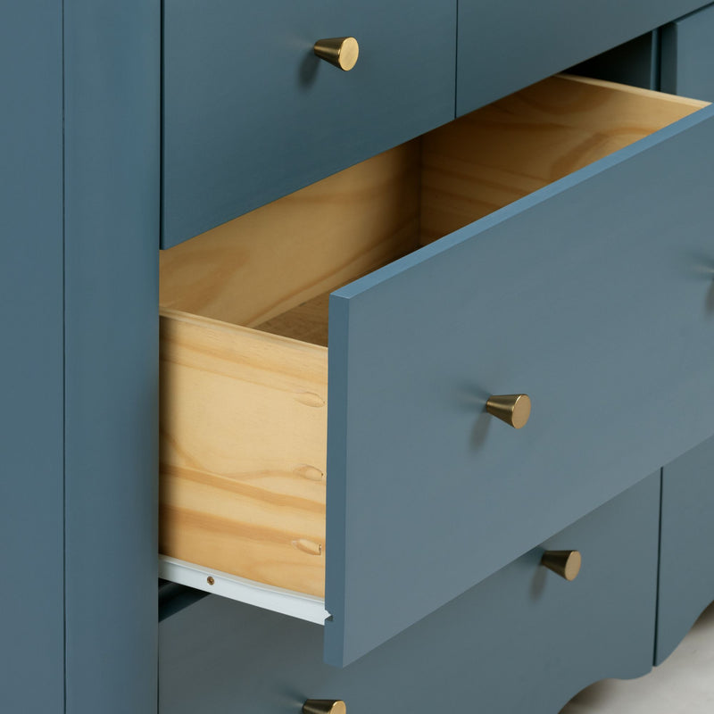 Close-up of a blue painted dresser with open drawers, brass cone knobs and natural wood interiors for modern bedroom storage