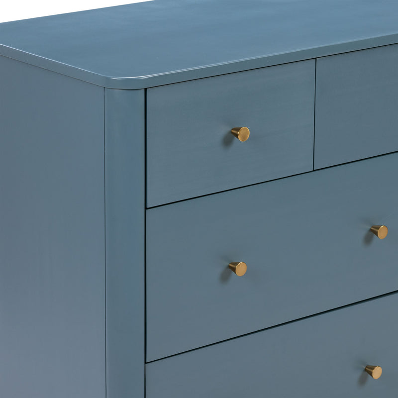 Close-up of blue painted wooden dresser with matte finish and round brass drawer knobs, modern bedroom storage furniture
