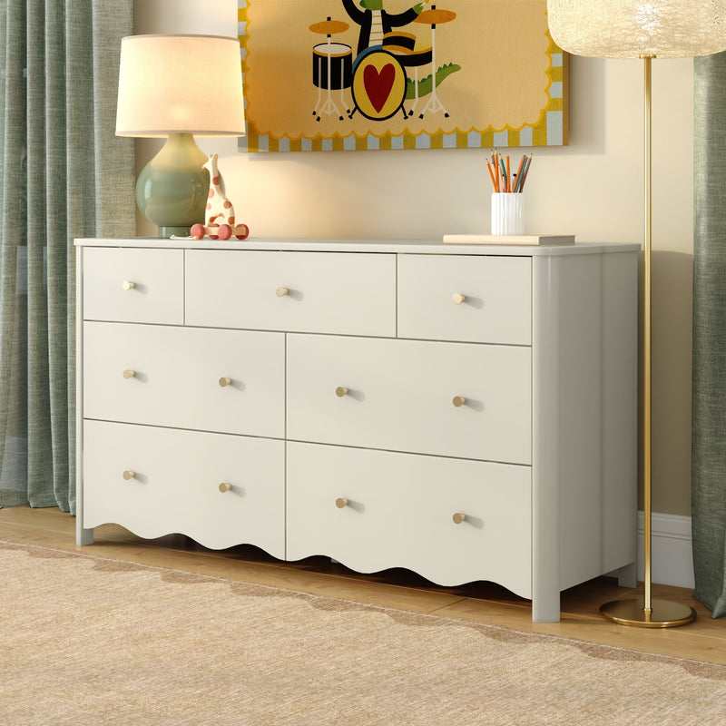 White nursery dresser with brass knobs, ceramic table lamp, wooden giraffe toy, pencil cup, colorful children's wall art and brass floor lamp