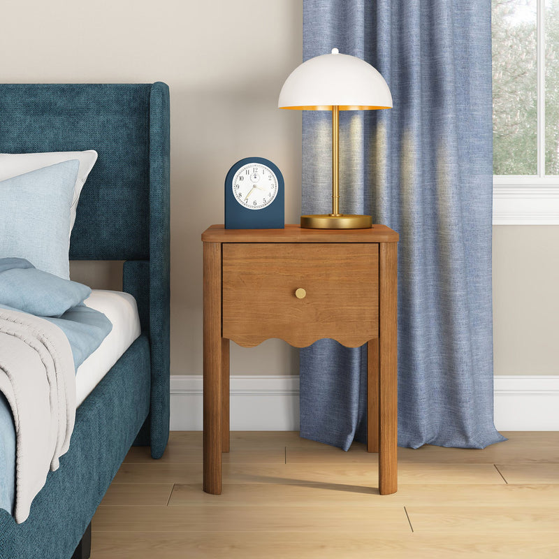 Wooden bedside table nightstand with gold-and-white modern table lamp, blue alarm clock beside teal upholstered bed and blue curtains in a cozy bedroom