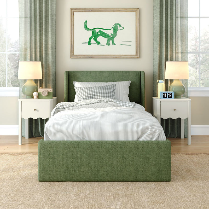 Green upholstered twin bed in cozy modern bedroom with white nightstands and table lamps, striped bedding and gingham pillow, green curtains, framed watercolor dog art above bed, natural light from windows