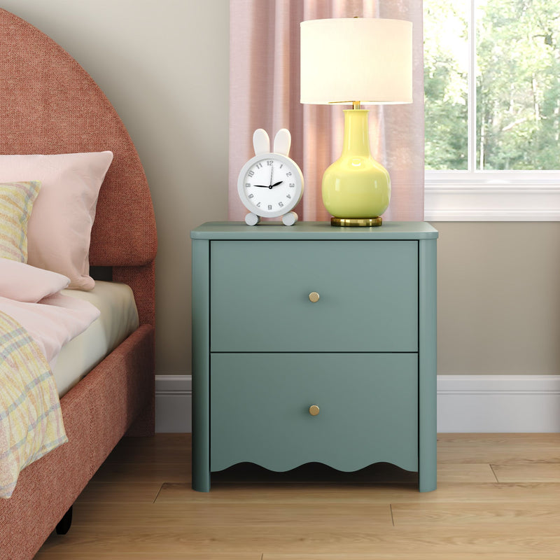 Modern teal two-drawer nightstand with brass knobs beside a pink upholstered bed, styled with a yellow ceramic table lamp and white bunny alarm clock in a bright bedroom