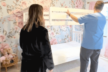 Couple assembling white bunk bed in a floral wallpapered bedroom for a chic nursery decor.