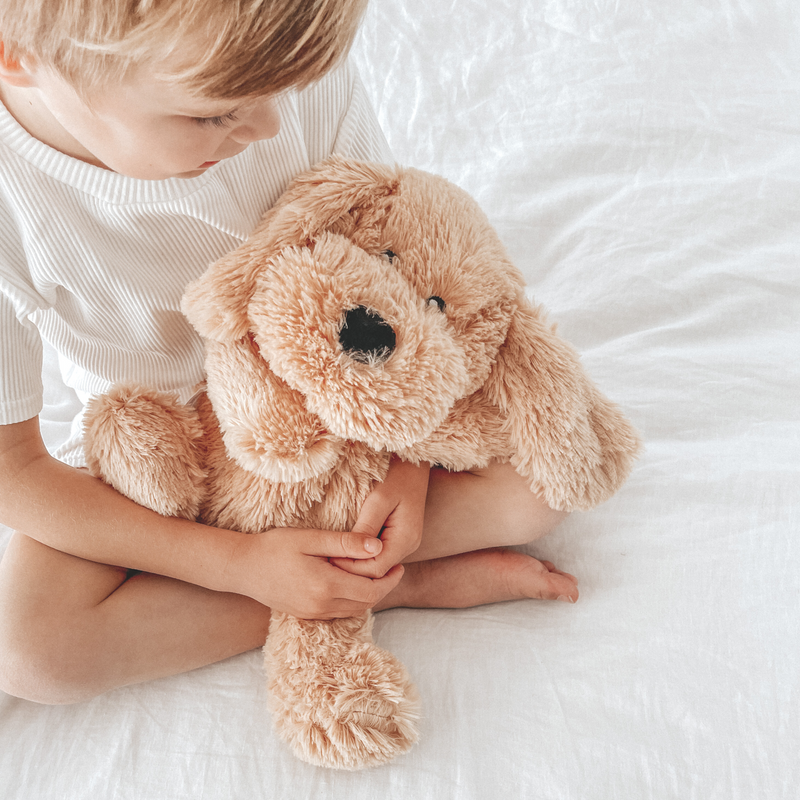 Child holding a soft plush teddy bear on a white bed, expressing comfort and coziness.