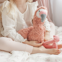 Child holding a pink flamingo plush toy while sitting on a bed in a cozy room.