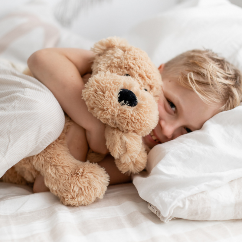 Child cuddling a brown teddy bear in bed with white sheets.
