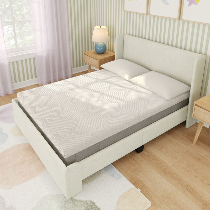Cream upholstered platform bed with white textured mattress topper and gray mattress in a bright modern bedroom with wooden nightstands, blue table lamp, and green striped wallpaper