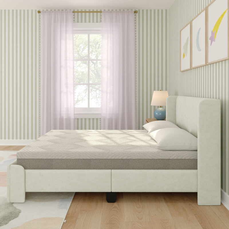 Cream upholstered platform bed with mattress and pillows in a pastel children's bedroom featuring green striped wallpaper, sheer curtains, wooden floor, patterned rug and blue bedside lamp