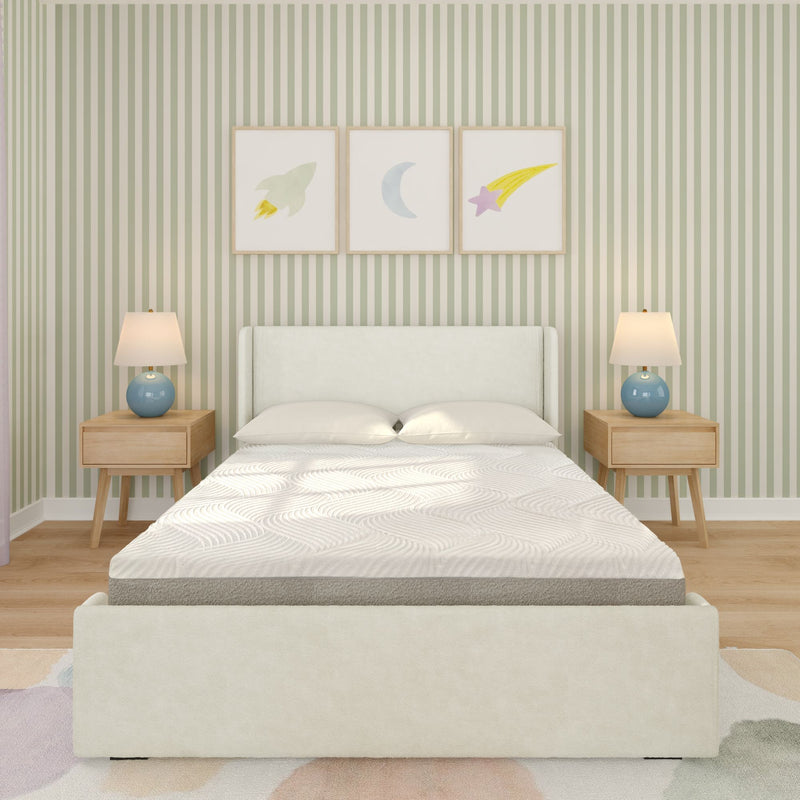 Children's bedroom with upholstered white bed, textured mattress, wooden nightstands with blue lamps, green striped wallpaper and framed rocket, moon and shooting star prints