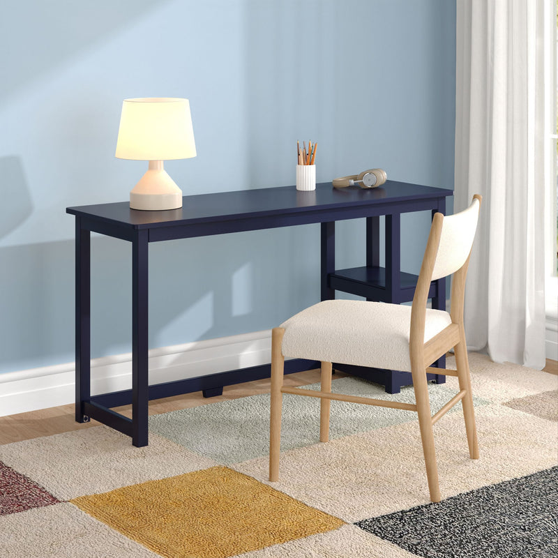 Minimal modern home office: navy desk with white table lamp, pencil holder, headphones, wooden chair, light blue wall and geometric rug