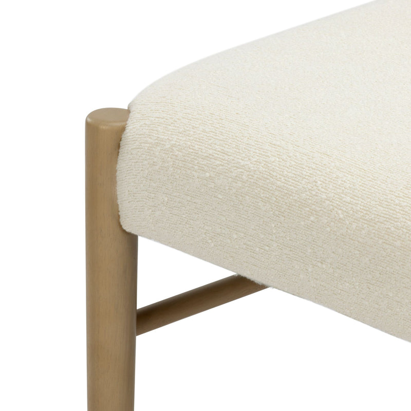 Close-up of cream boucle upholstered bench seat with rounded light oak leg and stretcher, modern minimalist dining bench in neutral fabric