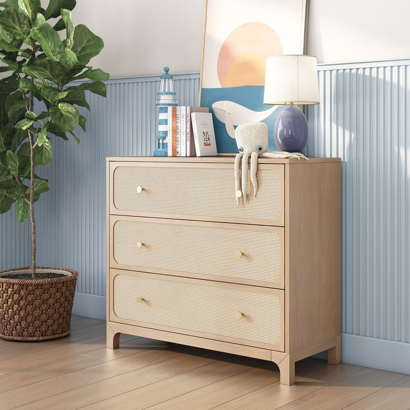 Light wood rattan-front three-drawer dresser in coastal nursery with blue beadboard wall, fiddle leaf fig plant, table lamp, books, plush octopus toy and whale wall art