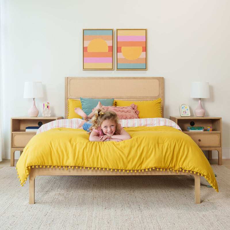 Smiling girl on yellow comforter in kids bedroom with wooden bed, colorful pillows, bedside lamps and abstract wall art