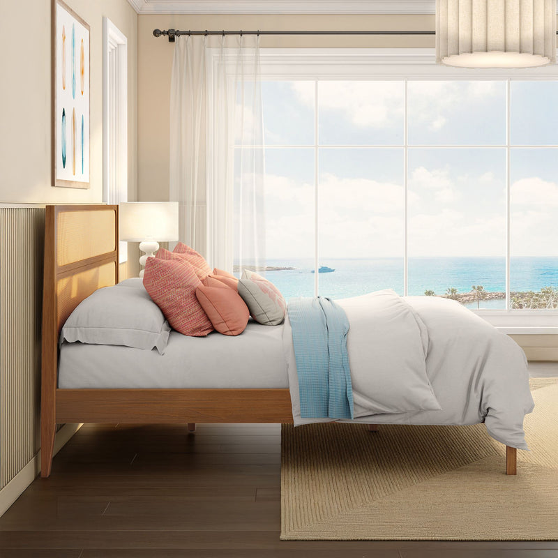 Modern coastal bedroom interior with wooden bed frame, layered coral and pastel pillows, sheer curtains and panoramic ocean view through large window