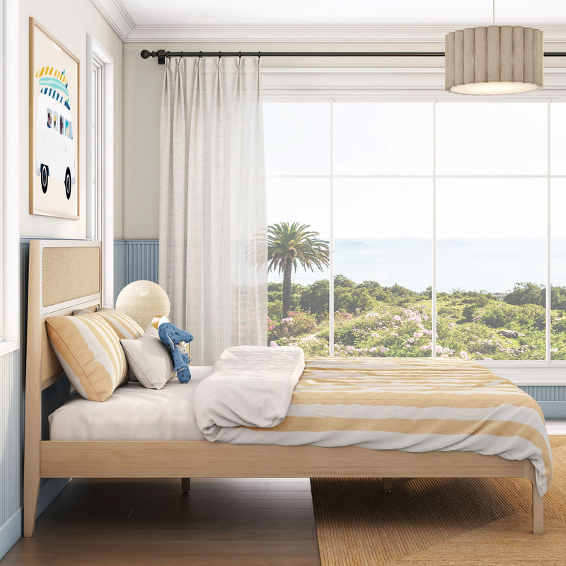 Coastal bedroom with light wood bed, yellow striped bedding, sheer curtains and large window framing palm tree ocean view