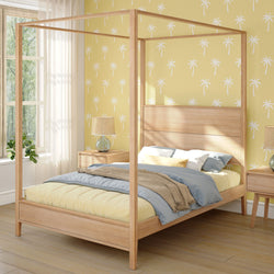 Four-poster wooden bed in a bright, modern bedroom with yellow palm tree wallpaper.