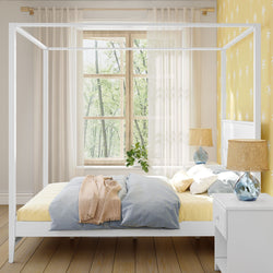 Elegant bedroom with a white canopy bed, yellow and blue bedding, natural light through a large window, and stylish decor.
